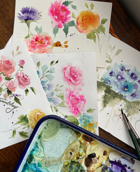 colourful watercolour florals on papers , a couple of paintbrushes and a butcher pan of paints